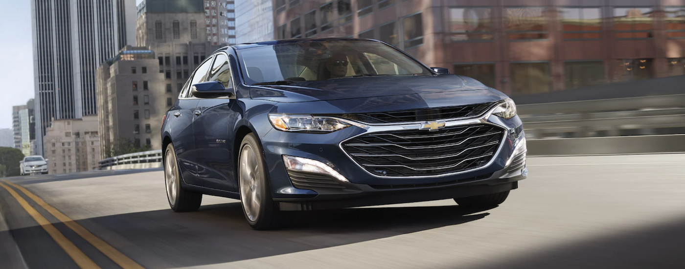 A dark blue 2022 Chevy Malibu driving through a city from a Chevrolet dealer near Bonner Springs.