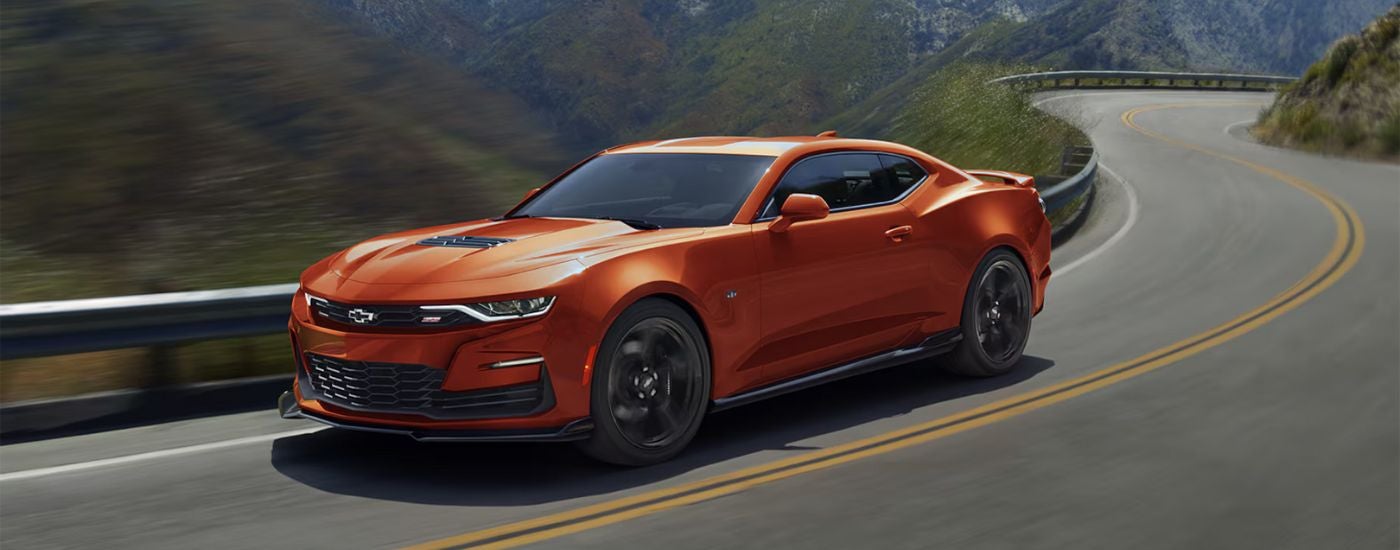 An orange 2024 Chevy Camaro 2SS driving on a winding highway to a Chevrolet dealer.
