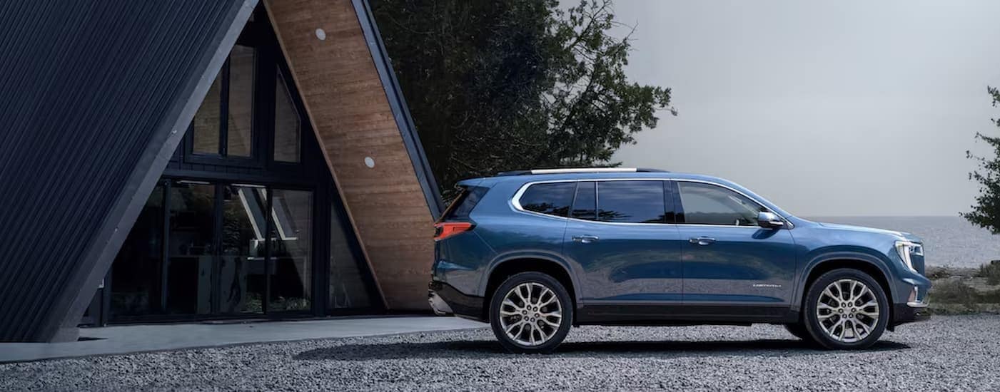 A blue 2025 GMC Acadia is parked near an A-frame cabin.
